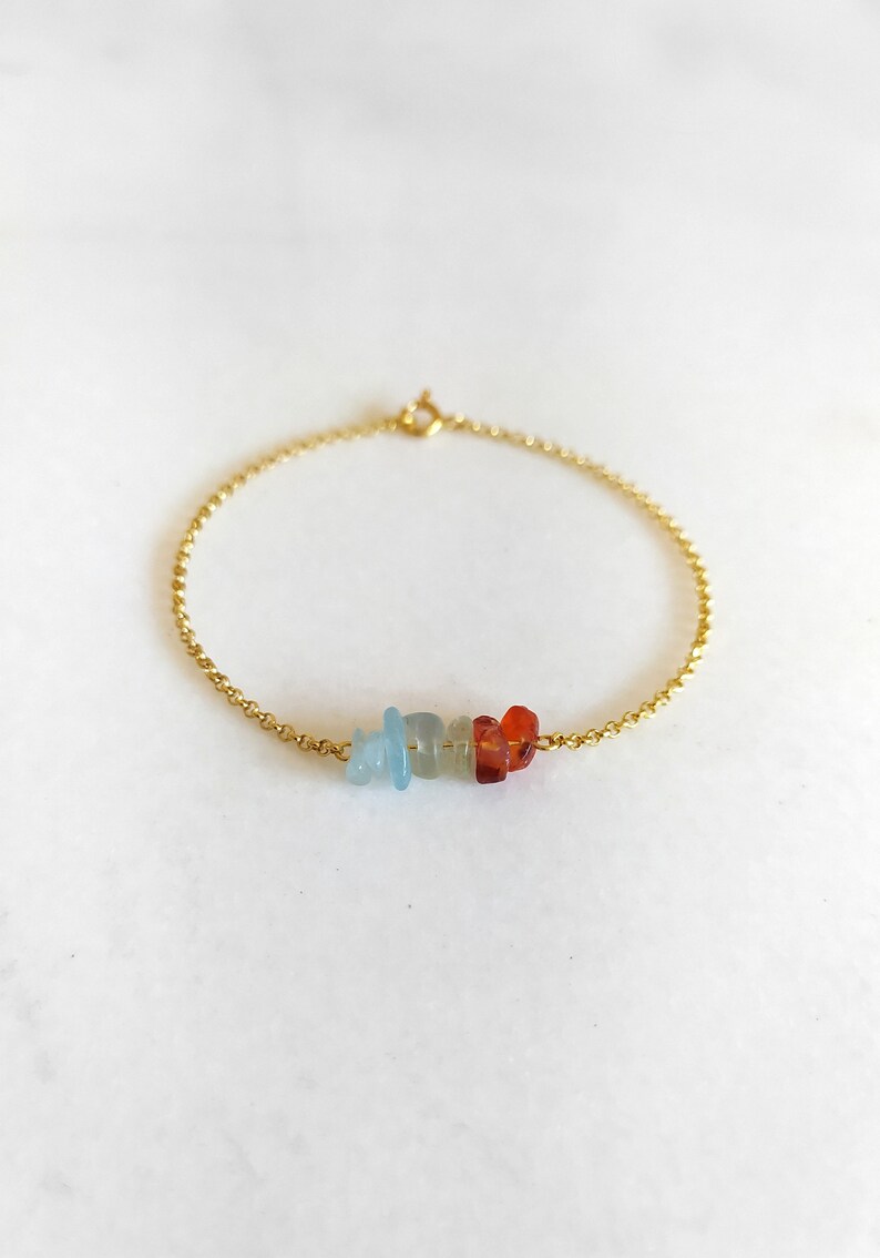 Peut inclure: Un bracelet en cha&icirc;ne dor&eacute;e avec une rang&eacute;e de petites pierres color&eacute;es. Les pierres sont bleues, vertes et orange.