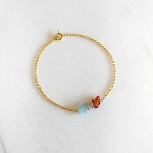 Peut inclure: Un bracelet en cha&icirc;ne dor&eacute;e avec une cha&icirc;ne d&eacute;licate et un groupe de petites pierres pr&eacute;cieuses bleu clair et orange.