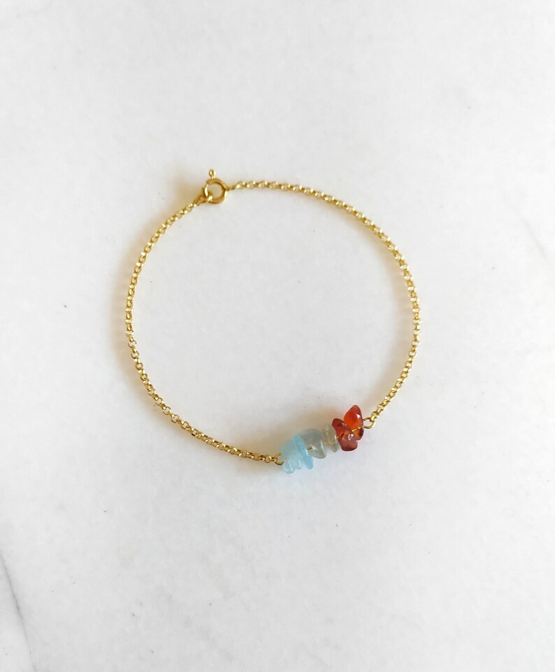 Peut inclure: Un bracelet en cha&icirc;ne dor&eacute;e avec une cha&icirc;ne d&eacute;licate et un groupe de petites pierres pr&eacute;cieuses bleu clair et orange.