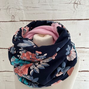 Könnte beinhalten: Ein marineblauer Infinity-Schal mit einem Blumendruck mit rosa, türkisfarbenen und weißen Blumen. Der Schal ist gefaltet und auf einer weißen Puppe ausgestellt.
