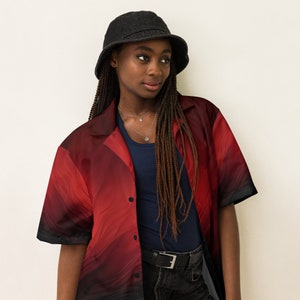 Op de afbeelding: Een persoon draagt een rood-zwart geprint overhemd met knopen, een zwarte bucket hat en een zwarte jeans.