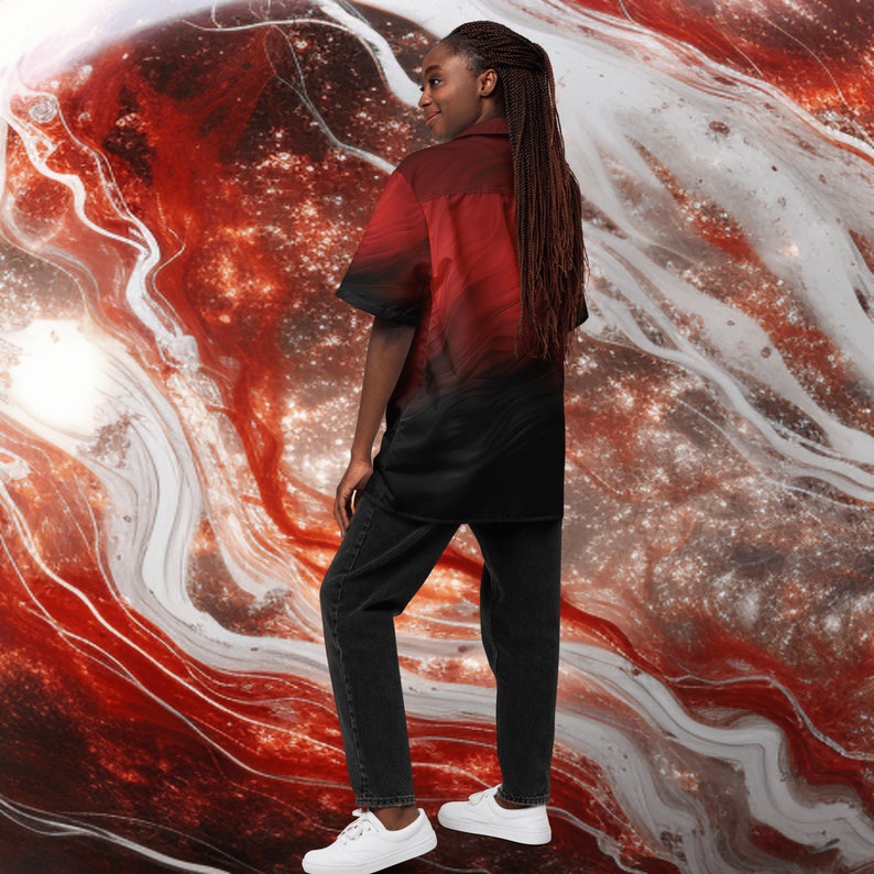Op de afbeelding: Een persoon draagt een rood en zwart knoopshirt met een galaxy print. Het shirt heeft een korte mouw en een kraag. De persoon draagt een zwarte broek en witte sneakers.