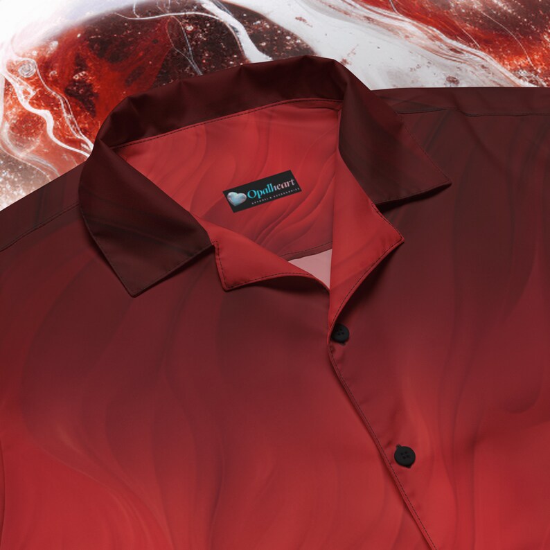 Op de afbeelding: Een rood overhemd met knopen, een verloopdessin en een klein label met de tekst "Opalheart" in een blauw hart. Het overhemd heeft een kraag en twee knopen.
