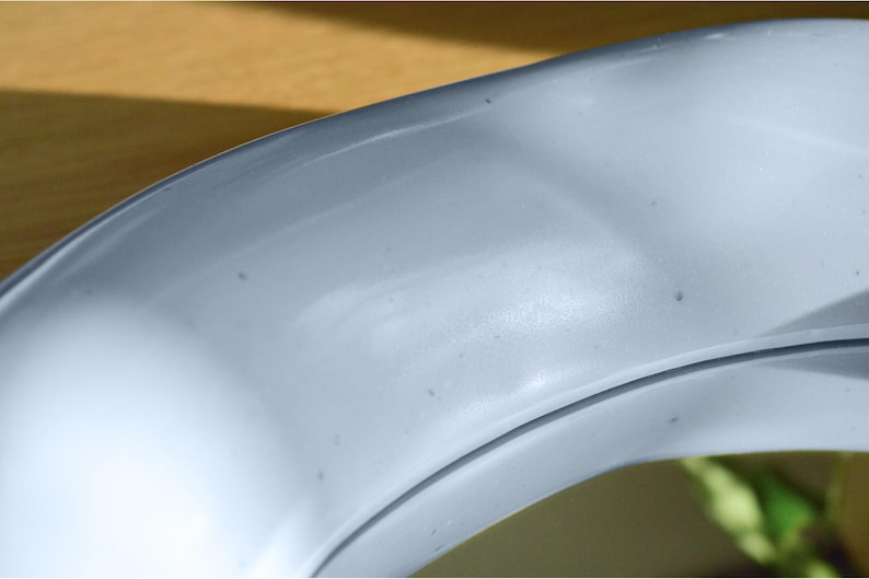 May include: Close-up of a curved, light blue object with a smooth, glossy surface. The object has a subtle sheen and appears to be made of a solid material. The image is well-lit, highlighting the curves and contours of the object.