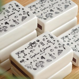 May include: A white ceramic mug with a black handle and the text "But First, Coffee" in a black, bold font. The mug is sitting on a white surface. The mug is approximately 4 inches tall.