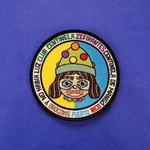 Puede incluir: Parche bordado redondo con una ilustración de dibujos animados de una persona con ojos grandes, que lleva un sombrero con lunares de colores. El parche tiene el texto "NO HABIA LUZ CLUB CENTINELA ZEFIRANTES CENTINELA DE MANGO OROCOVIS PUERTO RICO". El parche tiene un borde azul, amarillo y negro.