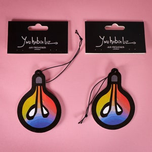 May include: Two air fresheners shaped like light bulbs with a colorful gradient design. Each bulb has a black border and a string for hanging. The packaging reads "Y no había Luz - AIR FRESHENER - LAVANDA".