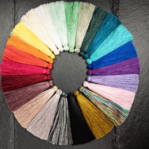 Puede incluir: Una carta de colores de 20 borlas de diferentes colores dispuestas en círculo sobre un fondo negro. Las borlas están hechas de un material suave y sedoso y están disponibles en una variedad de colores, incluyendo rojo, azul, verde, amarillo y morado.