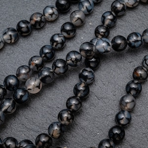 Puede incluir: Una hebra de cuentas de ágata negra y blanca. Las cuentas son redondas y tienen un acabado natural y pulido.