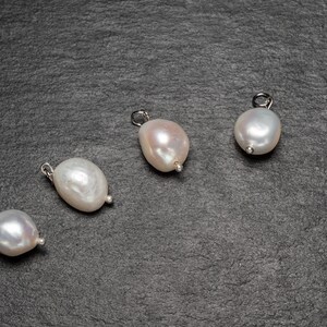 May include: Four white pearl pendants with silver clasps on a dark gray background.