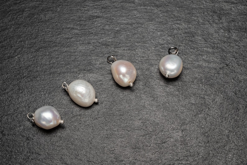 May include: Four white pearl pendants with silver clasps on a dark gray background.