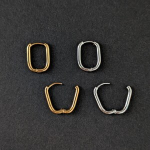 Può includere: Quattro paia di orecchini a cerchio in oro e argento sono esposti su uno sfondo scuro. Due paia sono rettangolari e due paia sono a forma di U. Gli orecchini hanno un design semplice e moderno, adatti all'uso quotidiano.