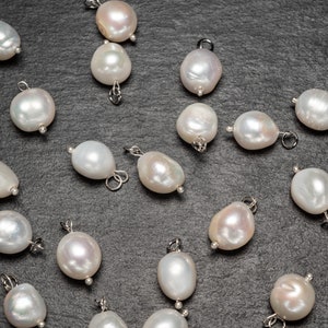 May include: A collection of white pearl charms with silver loops, scattered on a dark gray surface.
