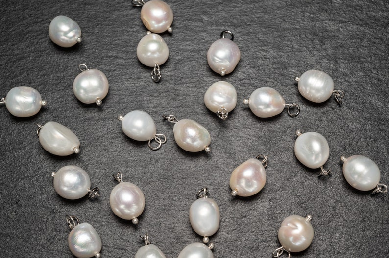 May include: A collection of white pearl charms with silver loops, scattered on a dark gray surface.