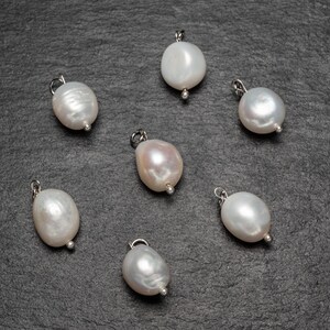 May include: Seven white pearl pendants with silver loops, arranged on a dark gray surface.