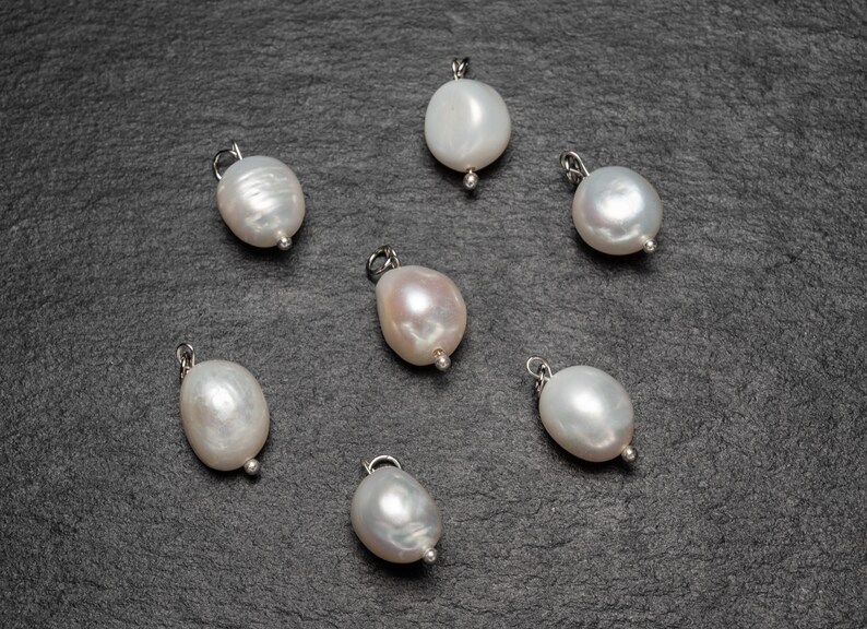 May include: Seven white pearl pendants with silver loops, arranged on a dark gray surface.
