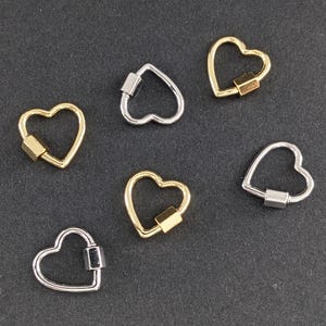 Könnte beinhalten: Sechs herzförmige Metallverschlüsse in Silber- und Goldtönen. Die Verschlüsse sind offen und haben einen quadratischen Steg in der Mitte.