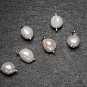 May include: Six white pearl charms with silver loops, displayed on a dark gray surface.