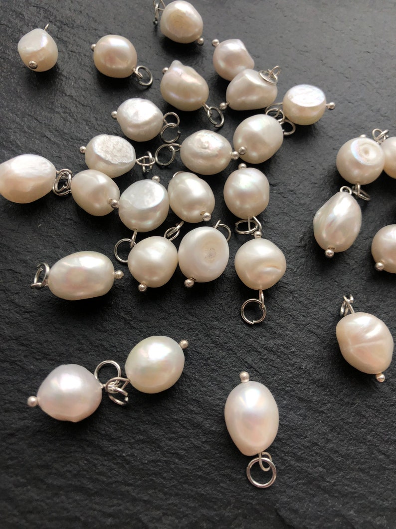 May include: A collection of white pearl charms with silver jump rings. The pearls are various shapes and sizes, and some have a slight iridescent sheen.