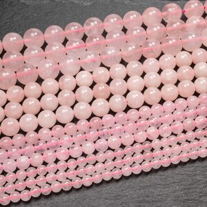 May include: A close-up of multiple strands of pink rose quartz beads. The beads are round and smooth, and they are arranged in a staggered pattern. The beads are strung on a thin, clear thread.