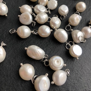 May include: A collection of white pearl charms with silver jump rings. The pearls are various shapes and sizes.