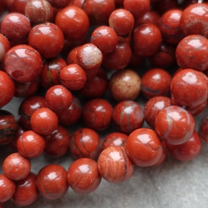 May include: A strand of red jasper beads with white and brown veins. The beads are round and smooth, and they are strung on a clear thread.