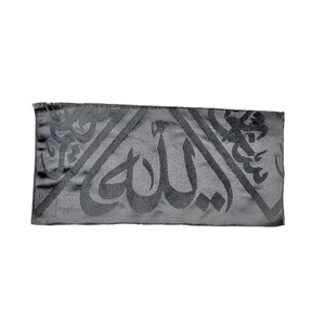 May include: A rectangular black scarf featuring a tonal woven pattern of Arabic calligraphy. The fabric has a subtle sheen and a smooth texture, with a fringed edge visible on the left side. The design consists of large, repeating script.