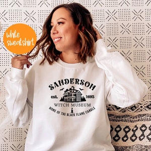May include: White sweatshirt with a black graphic print of a house with the text "Sanderson est. 1693 Witch Museum Home of the Black Flame Candle".
