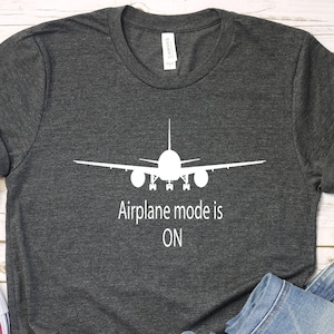 May include: A dark heather grey t-shirt with a white airplane graphic and the text "Airplane mode is ON".