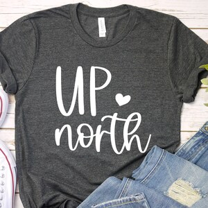 May include: A dark heather grey t-shirt with the text "UP north" in white with a small white heart.