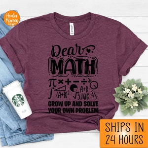 May include: A maroon t-shirt with a black graphic that says "Dear Math" with math symbols and the text "Grow up and solve your own problem".