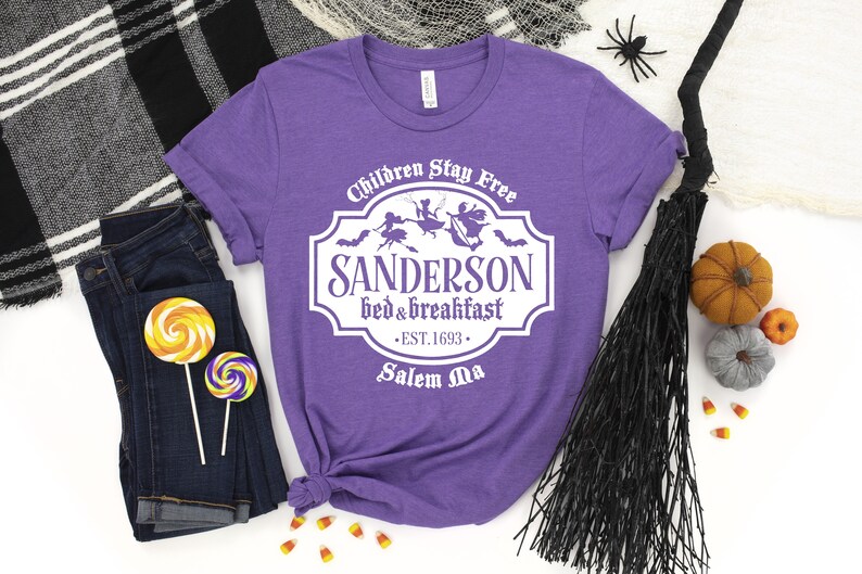 May include: Purple t-shirt with a white graphic of a sign that reads "Children Stay Free Sanderson Bed & Breakfast Est. 1693 Salem Ma".