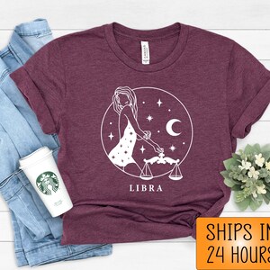 May include: A maroon t-shirt with a white graphic of a Libra zodiac sign. The graphic features a woman holding a scale and stars. The text "LIBRA" is printed below the graphic.