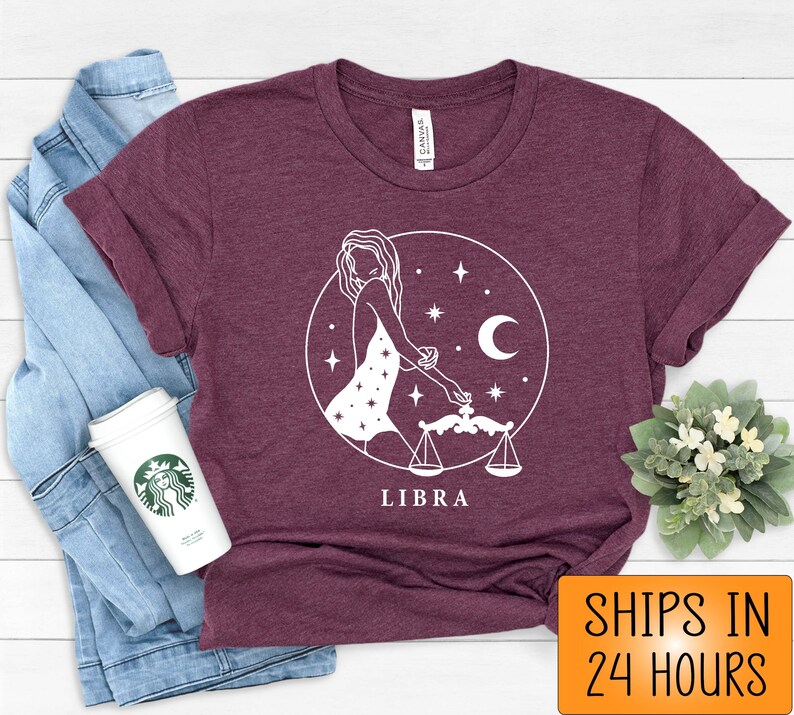 May include: A maroon t-shirt with a white graphic of a Libra zodiac sign. The graphic features a woman holding a scale and stars. The text "LIBRA" is printed below the graphic.