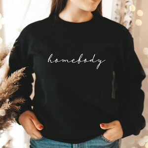 May include: Black sweatshirt with the text "homebody" written in white cursive script.