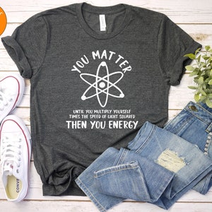 May include: A dark grey t-shirt with a white graphic of an atom and the text "You Matter Until You Multiply Yourself Times The Speed Of Light Squared Then You Energy".