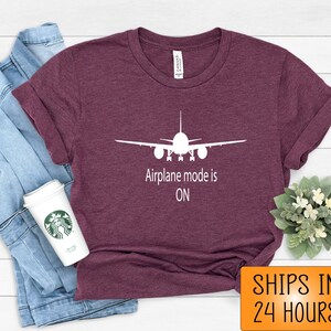 May include: A maroon t-shirt with a white airplane silhouette and the text "Airplane mode is ON".