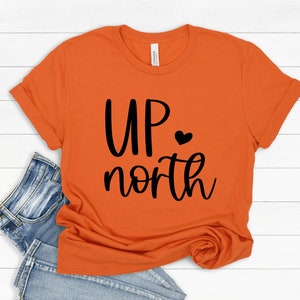 May include: Orange short-sleeved t-shirt with black text that reads "UP north" with a small black heart.