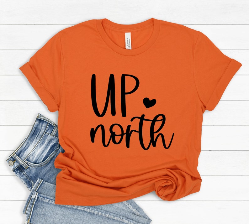 May include: Orange short-sleeved t-shirt with black text that reads "UP north" with a small black heart.