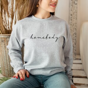 May include: A gray sweatshirt with the text "homebody" written in black cursive on the front.