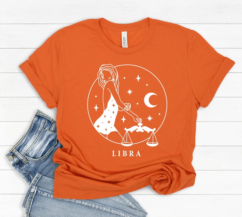 May include: Orange t-shirt with a white graphic of a woman with a Libra zodiac symbol and the word "LIBRA" printed below.