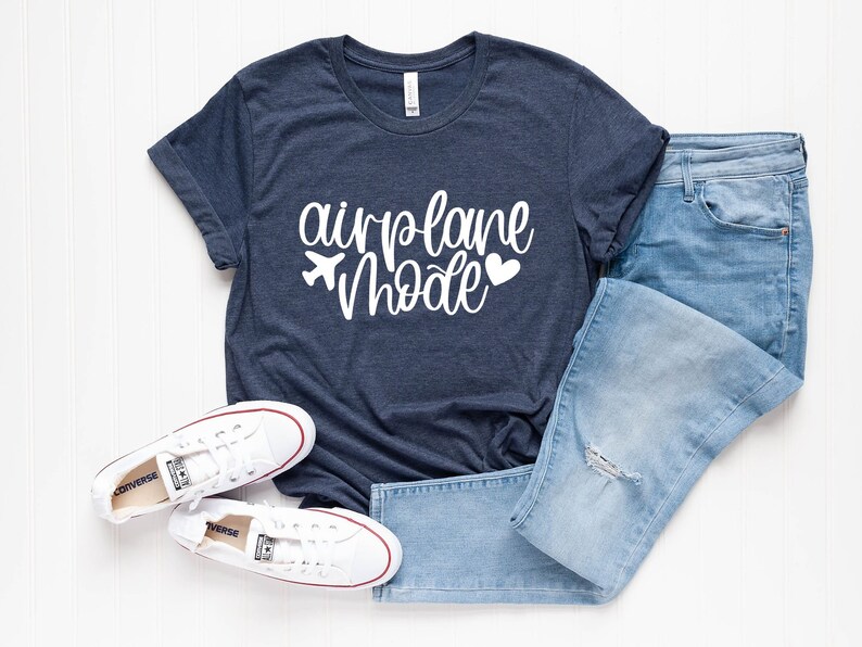 May include: A navy blue t-shirt with white text that reads "airplane mode" with a small airplane and heart graphic. The shirt is paired with blue jeans and white sneakers.