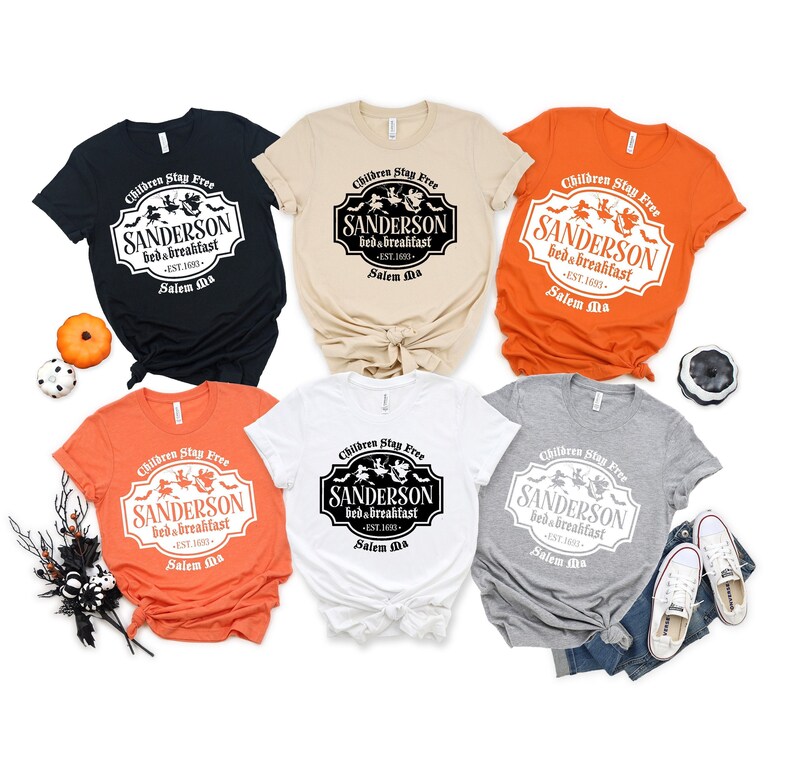 May include: Six t-shirts in different colors with a white graphic print of a sign that reads "Children Stay Free Sanderson Bed & Breakfast - Est. 1693 - Salem Ma".
