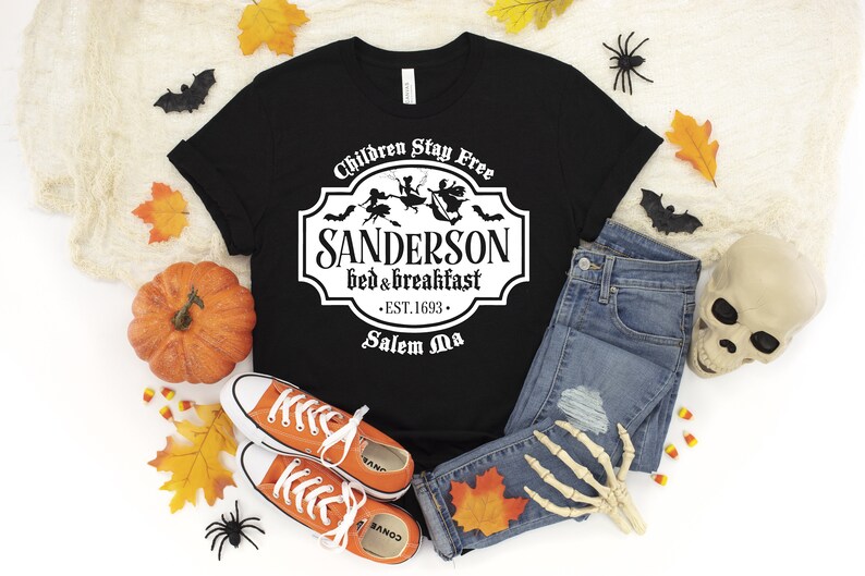 May include: Black t-shirt with a white graphic of a sign that says "Sanderson Bed & Breakfast - Est. 1693 - Salem Ma" with a witch and bats flying around it. The text above the sign says "Children Stay Free".