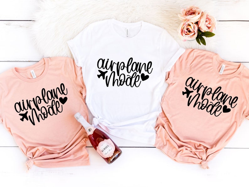 May include: Three t-shirts with the text "airplane mode" in black script with a small airplane icon and heart. Two shirts are peach colored and one is white.