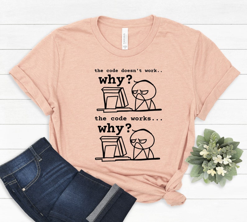 May include: A peach-colored t-shirt with a black and white illustration of a stick figure at a computer. The text on the shirt reads "the code doesn't work... why?" and "the code works... why?"