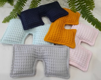 May include: A collection of six U-shaped pillows featuring a textured waffle weave fabric. The pillows are available in navy blue, mustard yellow, light blue, light pink, and gray, each with a distinct cutout section in the center of the bottom edge.
