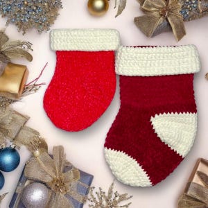 Könnte beinhalten: Zwei rot-weiße gehäkelte Weihnachtssocken. Der größere Socken hat einen weißen gehäkelten Bund und eine weiße gehäkelte Spitze. Der kleinere Socken hat einen weißen gehäkelten Bund.