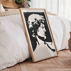 May include: A black and white print of a man's face in profile, framed in a light wood frame. The print is hanging on a white wall in a bedroom setting.