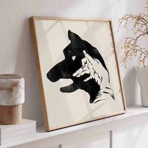Puede incluir: Una impresión enmarcada de una silueta en blanco y negro de una mano haciendo una sombra de la cabeza de un perro.